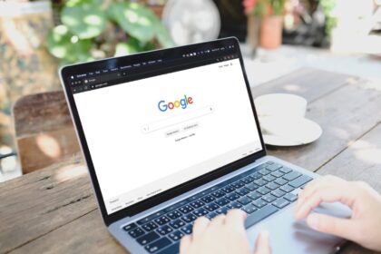 Pessoa usando um notebook com a página inicial do Google aberta, em um ambiente externo, sugerindo busca online por informações.