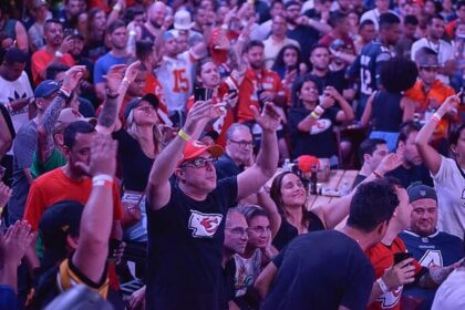 Torcedores lotam o Armazém 3 do Pier Mauá durante o Super Bowl LX Experience, no Rio de Janeiro, vibrando com a transmissão ao vivo da NFL, muitos vestidos com camisas de franquias como Kansas City Chiefs e San Francisco 49ers, em clima de festa e celebração do futebol americano.